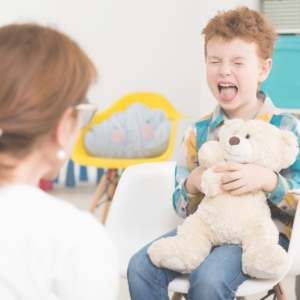 a young child is highly sensitive and emotional as he holds a bear and cries with a lady counselor